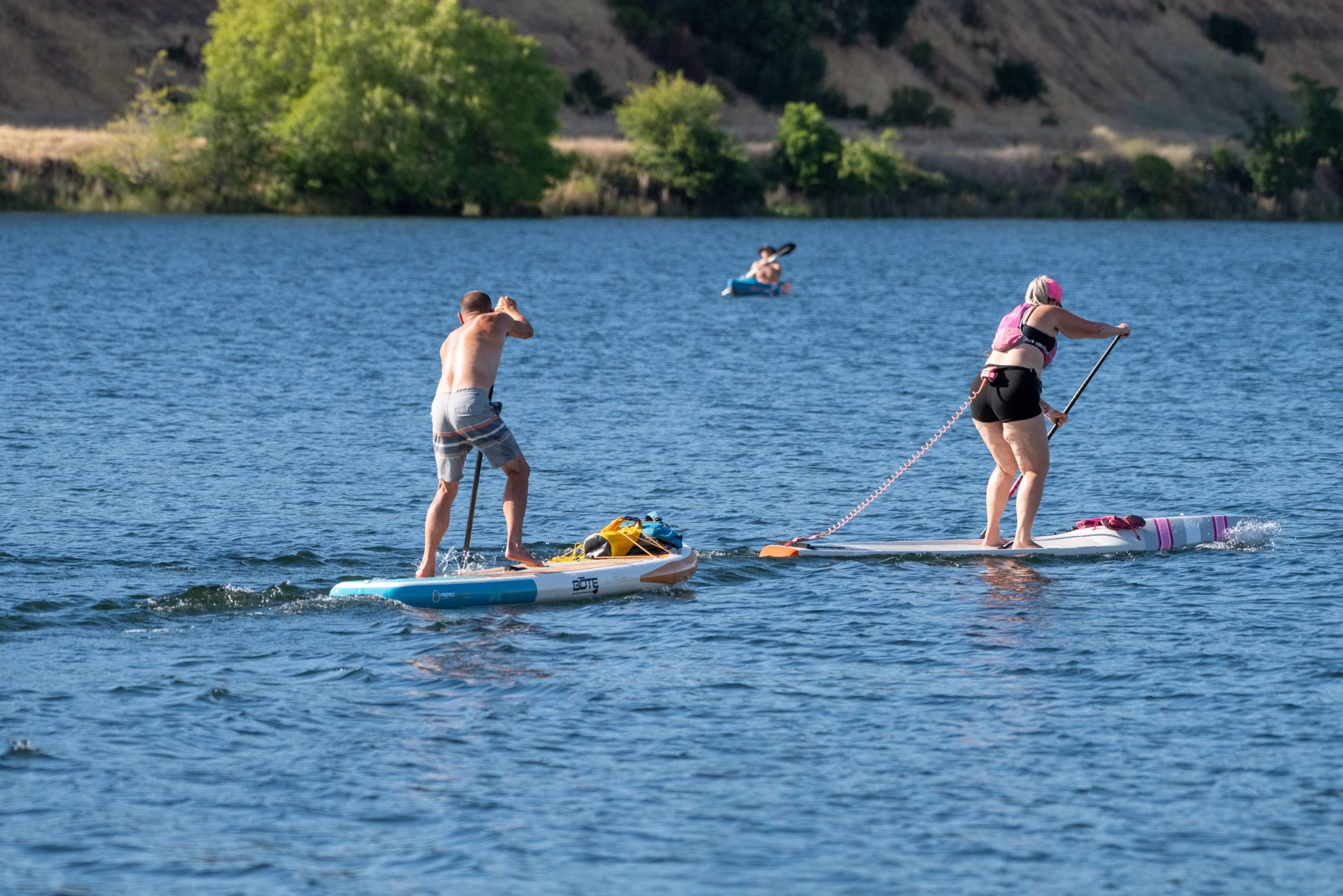 Two paddle boarders and a kayaker on lake natoma during a summer time trial session