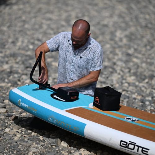 Paddler inflating a bote inflatable sup with an outdoormaster electric pump on a rocky shoreline