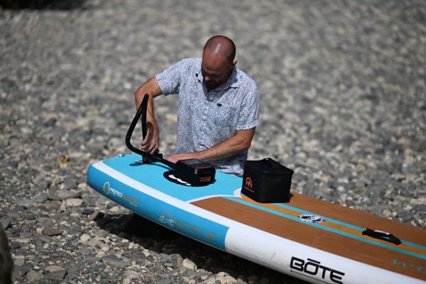 Paddler inflating a bote inflatable sup with an outdoormaster electric pump on a rocky shoreline