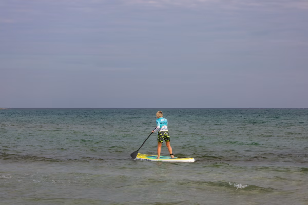 Stand-up paddleboarder mid-stroke on calm open water, torso rotated and top arm extended at the catch