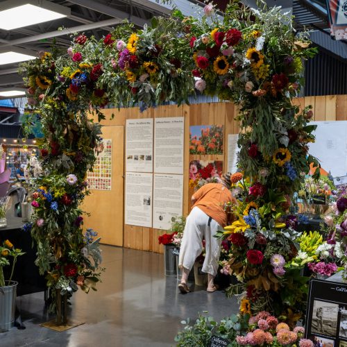 At the california state fair, a wall of flowers tells one of california's stories 5 in pavilion b at the california state fair, tucked behind the livestock barns, there is an archway built entirely of flowers. Sunflowers and dahlias, roses and protea, blue delphinium spilling over orange ranunculus, and every stem of it grown somewhere in california. A working flower shop sits underneath the arch. Behind it stands a wall of old photographs and hand-lettered signs. A floral archway of california grown flowers over the history display at the california state fair