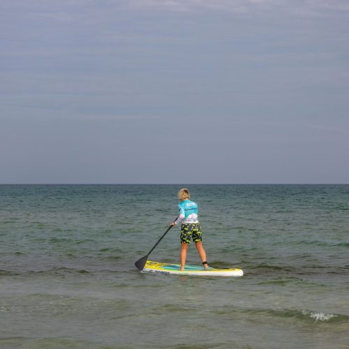 Stand-up paddleboarder mid-stroke on calm open water, torso rotated and top arm extended at the catch