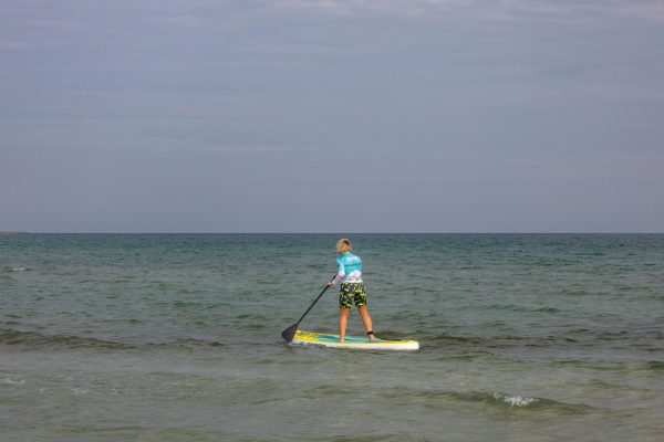 Stand-up paddleboarder mid-stroke on calm open water, torso rotated and top arm extended at the catch