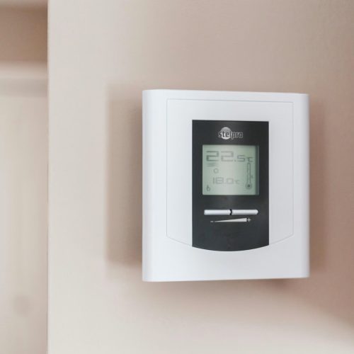 White smart thermostat mounted on a wall, displaying temperature in a residential home