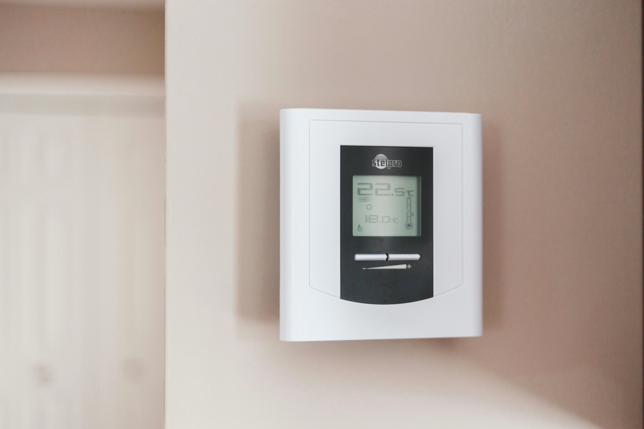 White smart thermostat mounted on a wall, displaying temperature in a residential home
