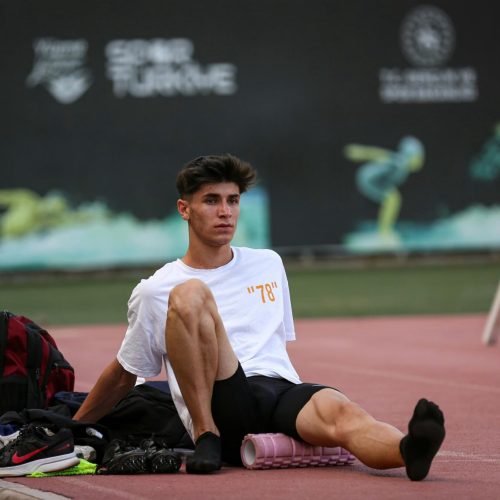 Athlete in sportswear using a foam roller on a track after training to massage the leg