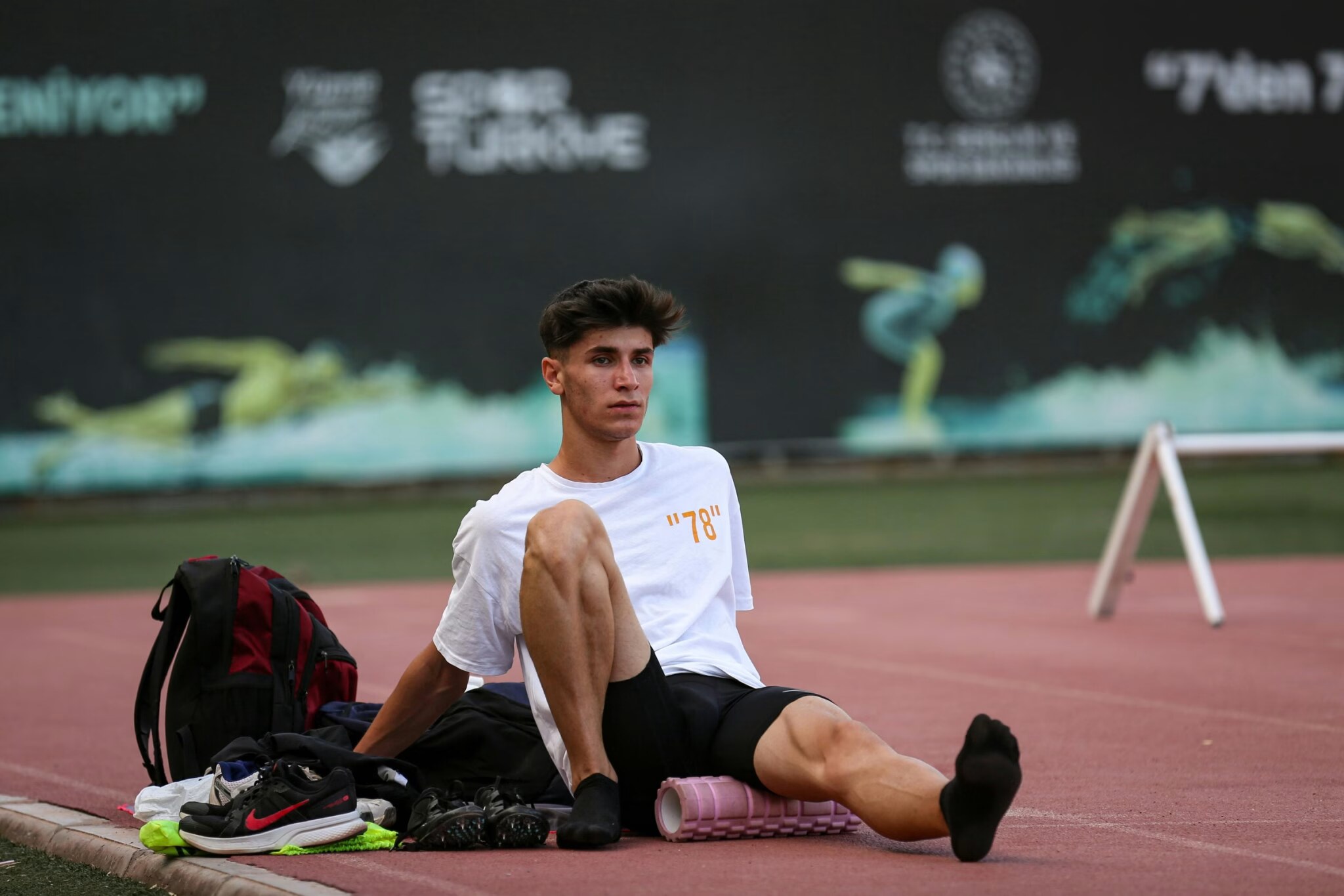 Athlete in sportswear using a foam roller on a track after training to massage the leg