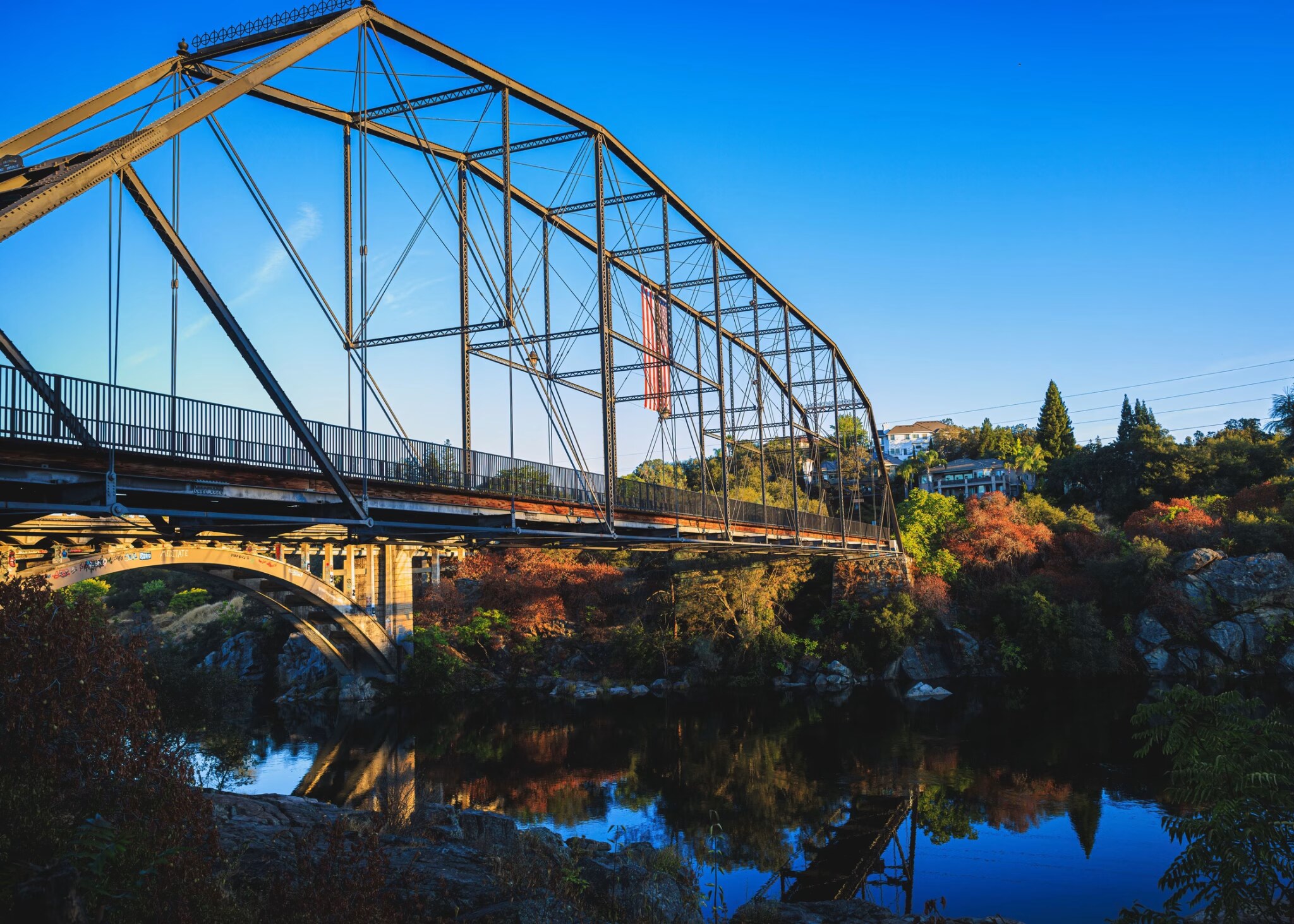 Historic truss bridge over the american river in folsom, california, with fall foliage along the banks