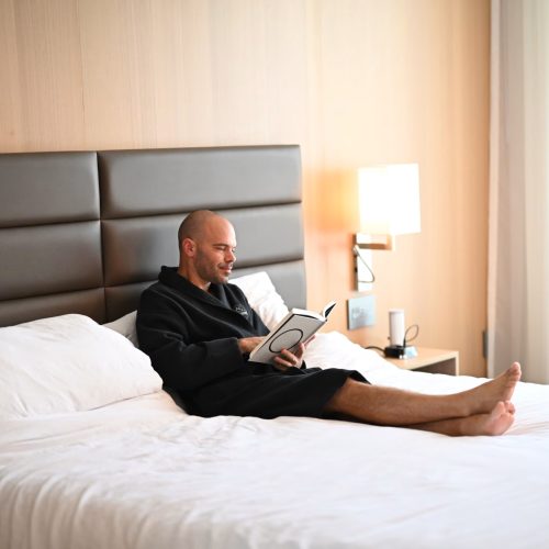 Michael kahn in a hotel robe, sitting up in bed reading a book, the same kind of sick-day research session that produced this probiotic-antibiotic guide