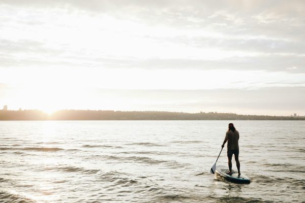 Paddle boarder silhouette on calm water at sunset, paddle in hand, illustrating the sustained grip and arm positioning that loads peripheral nerves during long sessions