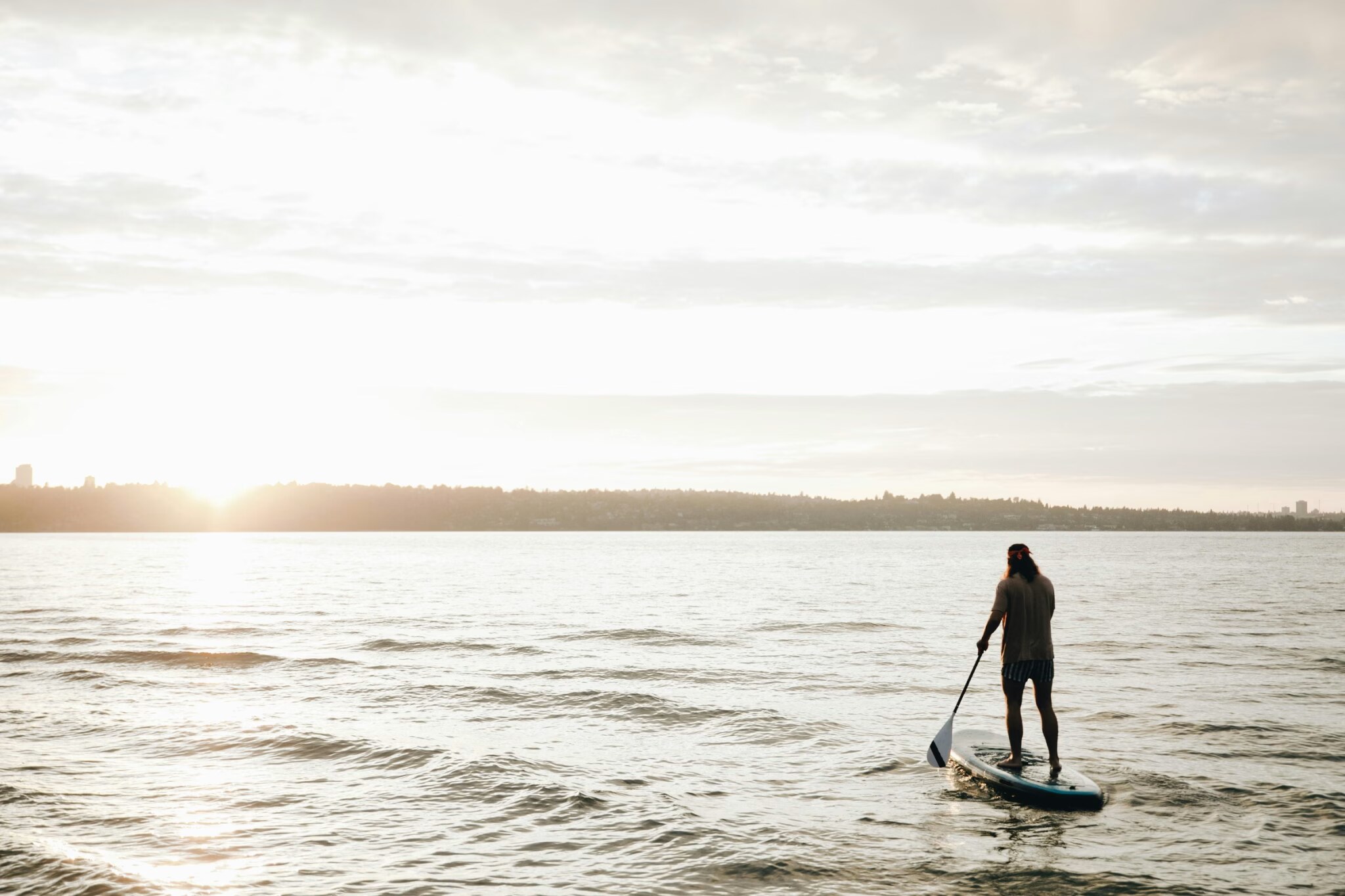 Paddle boarder silhouette on calm water at sunset, paddle in hand, illustrating the sustained grip and arm positioning that loads peripheral nerves during long sessions