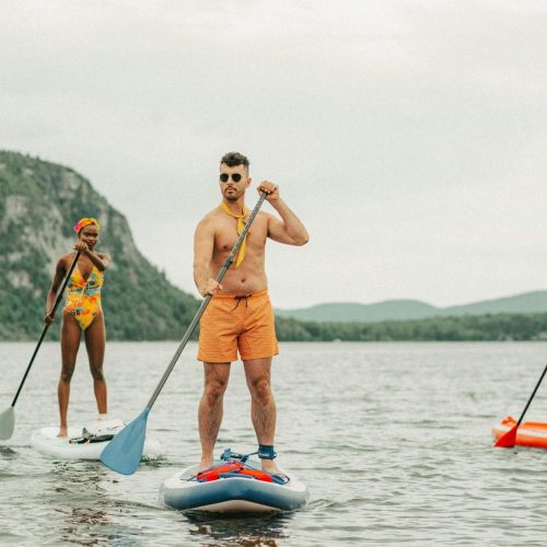 Three stand-up paddlers on a flatwater lake, the central paddler gripping a vertical paddle shaft with hands at shoulder-width spread