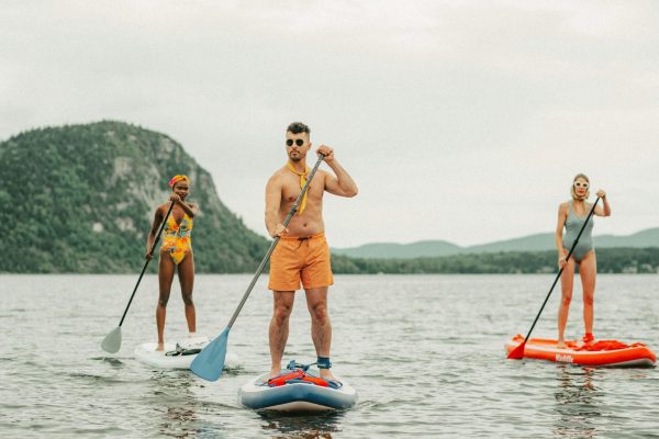 Three stand-up paddlers on a flatwater lake, the central paddler gripping a vertical paddle shaft with hands at shoulder-width spread