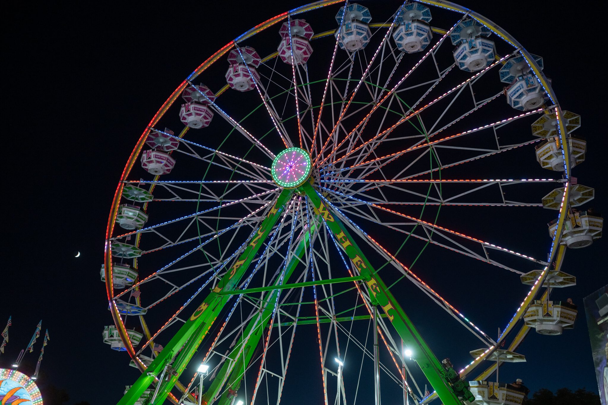 The giant ferris wheel lit up at night against a crescent moon at the california state fair