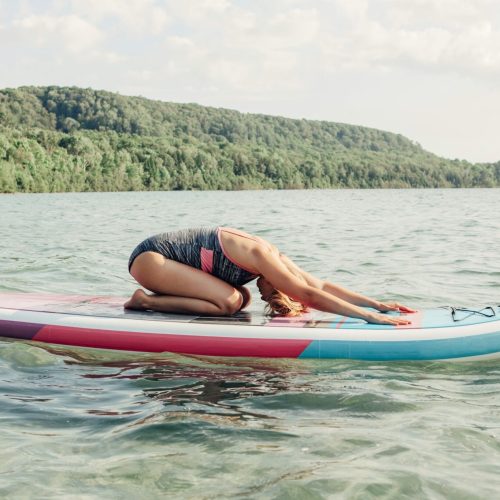 Woman in child's pose stretching on a paddle board on a calm forested lake
