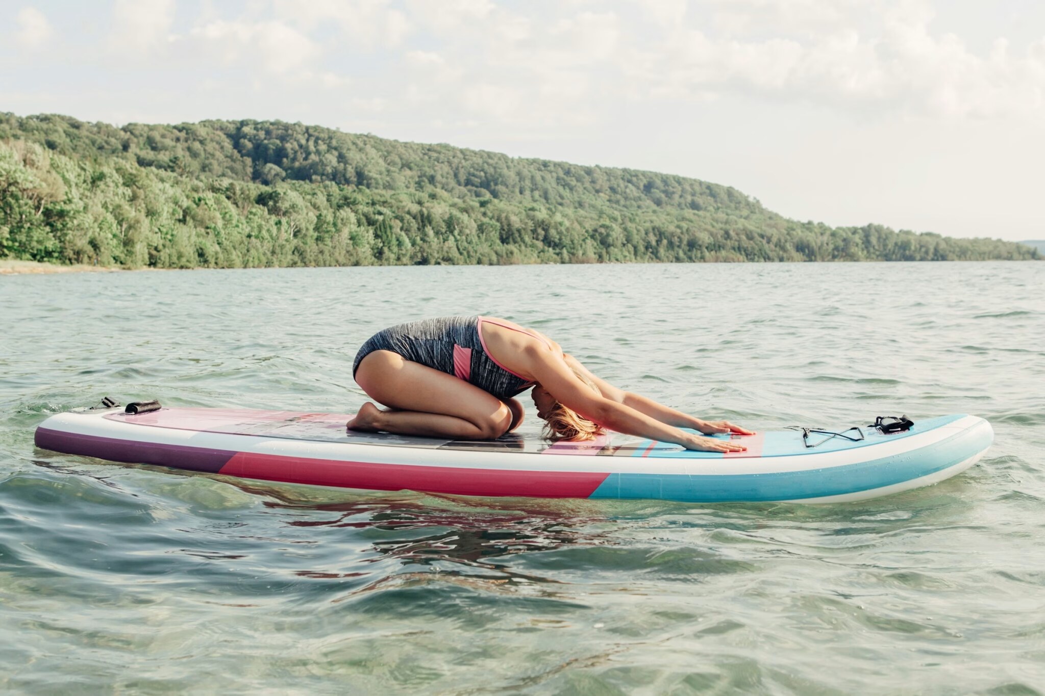 Woman in child's pose stretching on a paddle board on a calm forested lake