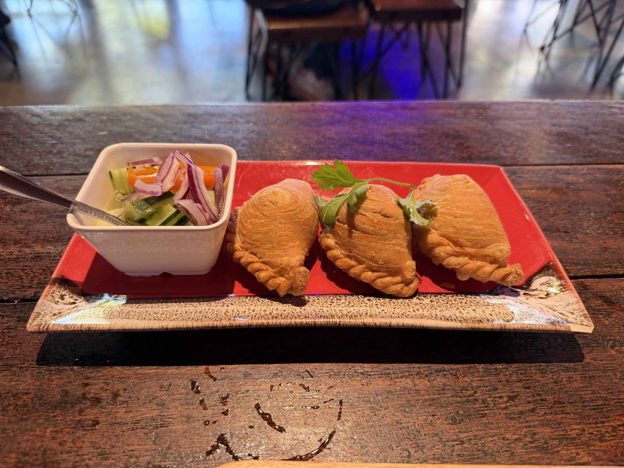 Three chicken curry puffs on a red lacquer tray with cucumber relish at kin thai street eatery in sacramento