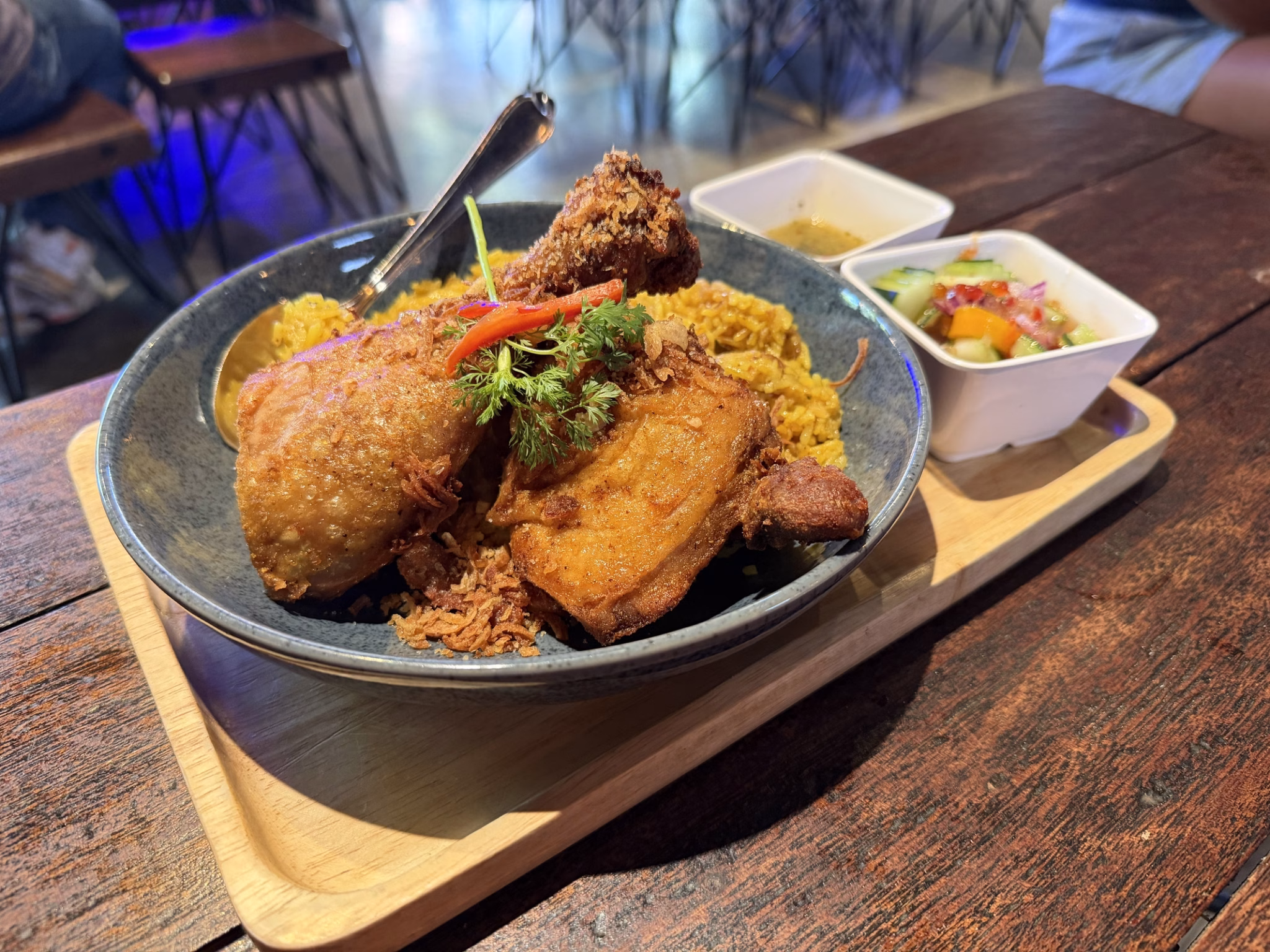 Khao mok gai tod, fried chicken over turmeric biryani rice in a blue bowl with dipping sauce and cucumber relish at kin thai street eatery