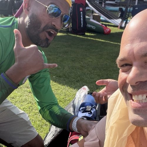 Michael kahn smiling on the grass at usa sup nationals in gig harbor with his right arm wrapped and a sling tied at his chest, while carl, a nurse practitioner on the event medical team, holds the wrap and gives a shaka