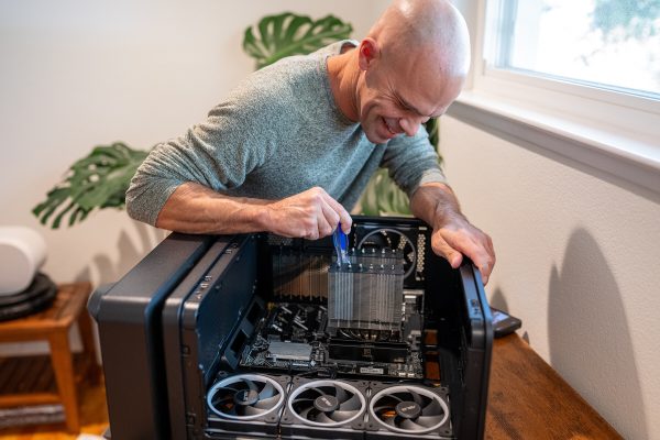Michael kahn smiles as he screws a thermalright dual-tower heatsink onto the motherboard inside an asus prime ap304 case lying on its side