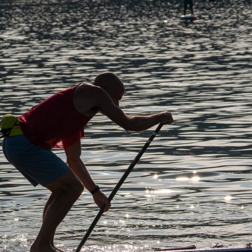 Silhouette of a stand-up paddler bent into a stroke with both hands on the paddle shaft against sunlit water at the 2026 usa sup national championships