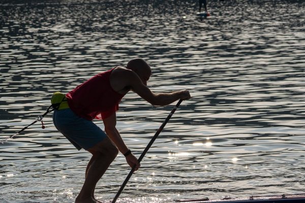 Silhouette of a stand-up paddler bent into a stroke with both hands on the paddle shaft against sunlit water at the 2026 usa sup national championships