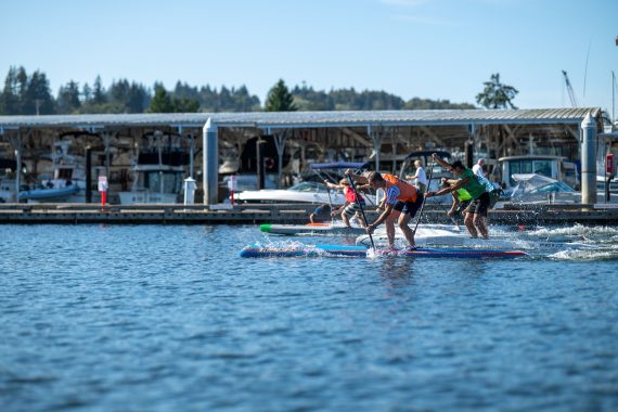 Three paddlers sprinting race boards past the Gig Harbor docks